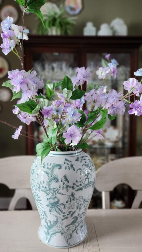 green and white ginger jar on dining table with purple flowers inside