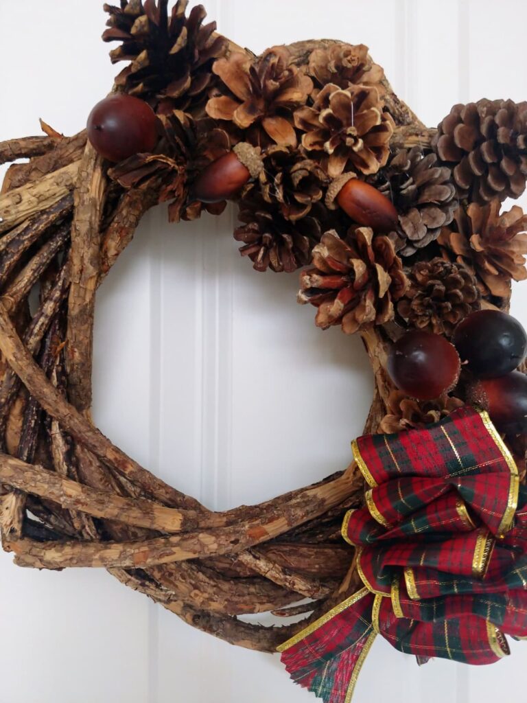 grapevine wreath with pinecones on it and red plaid ribbon