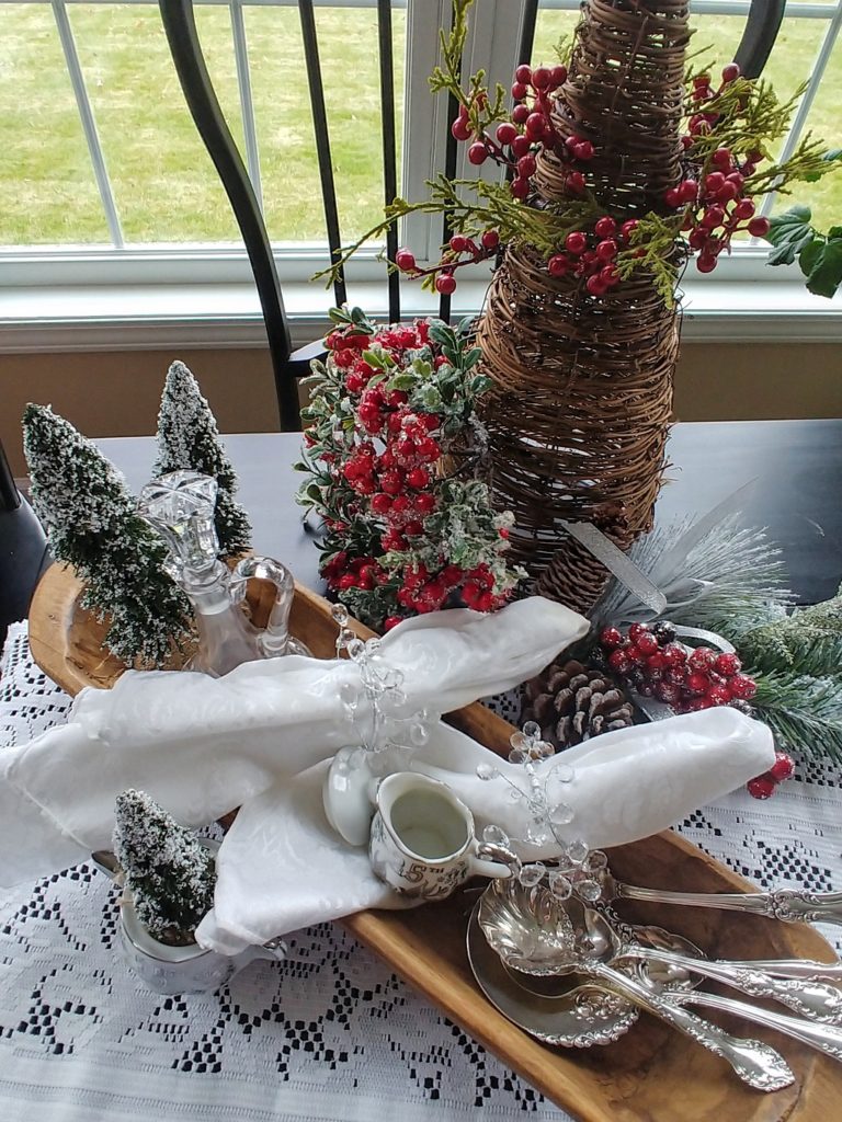 a wooden dough bowl filled with bottle brush trees and white cloth napkins