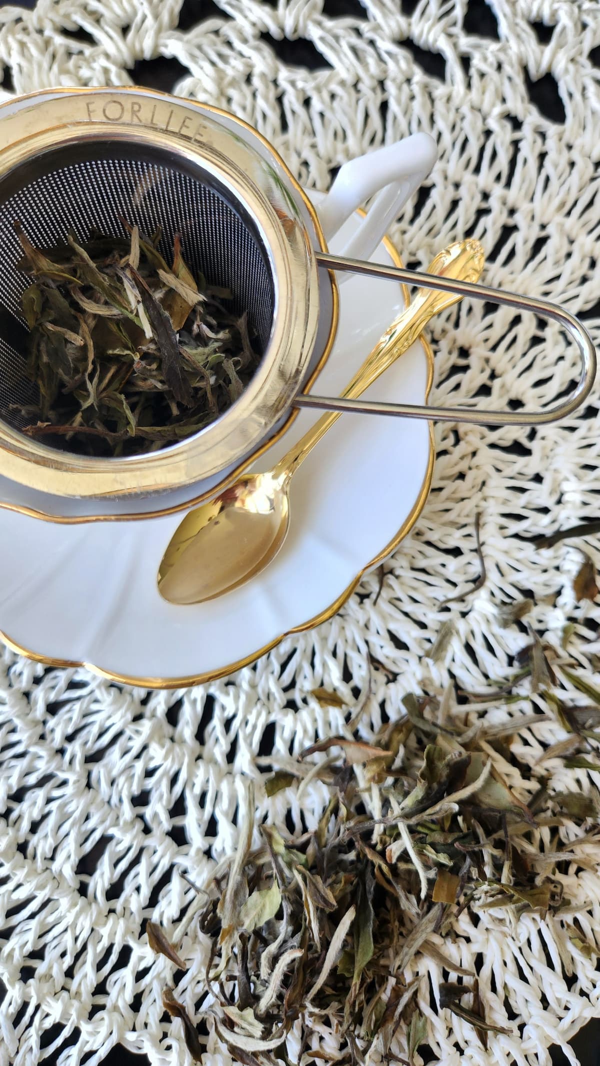 tea being steeped in an infuser in white tea cup with gold rim