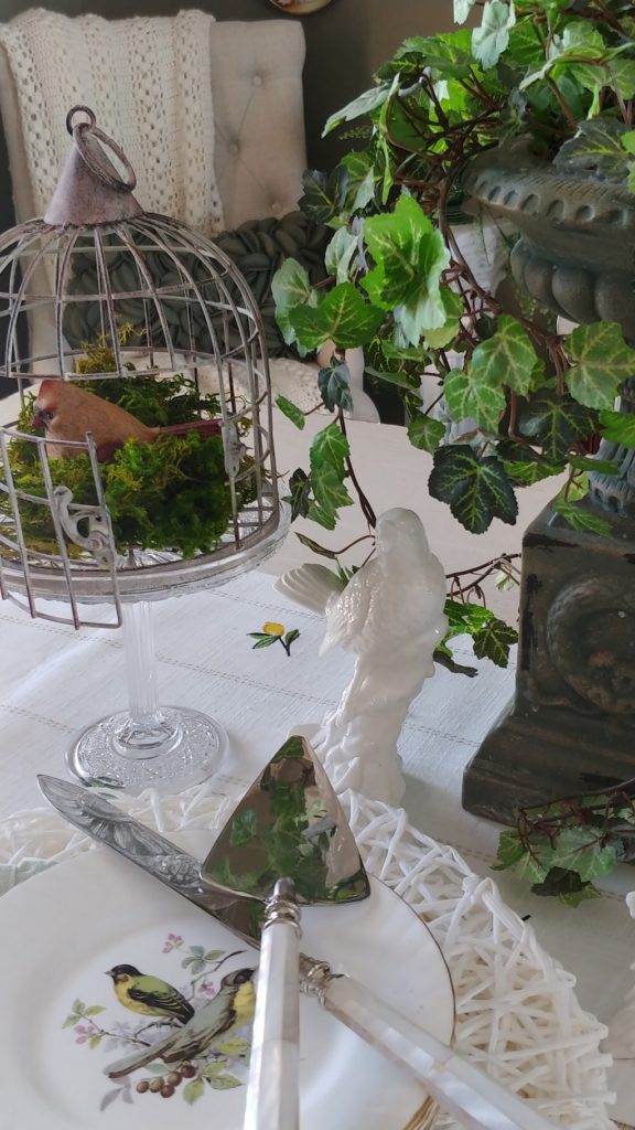 A plate topped with a vase of flowers on a table, with a birdcage and Plant