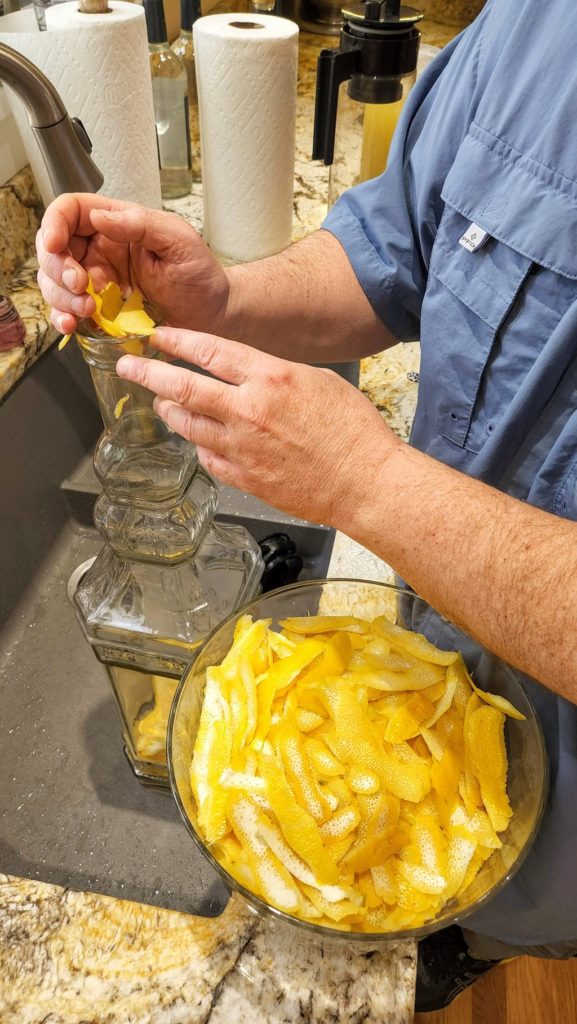 Hands putting lemon peels in a glass vat