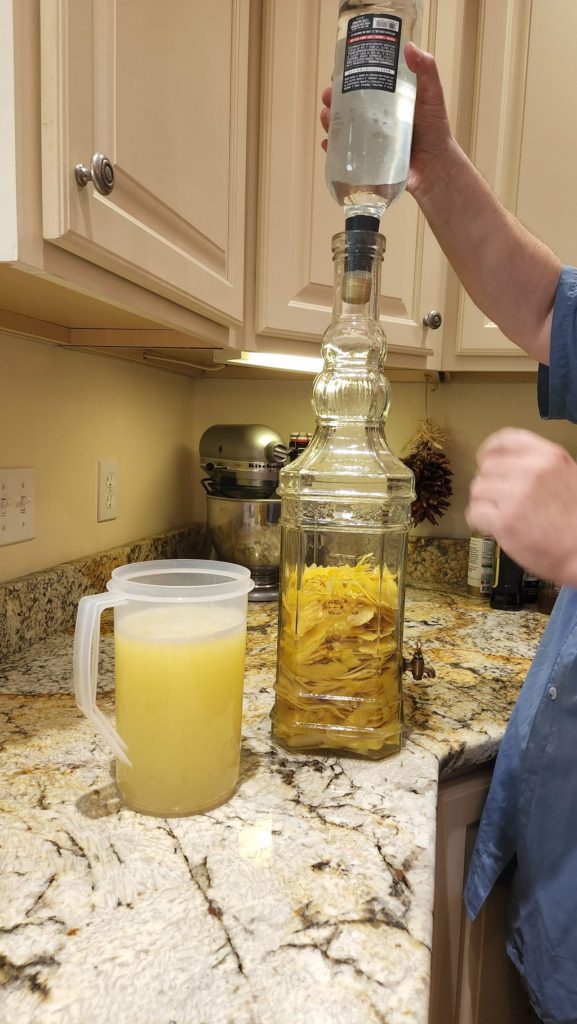 Pouring vodka into glass vat with lemon peels