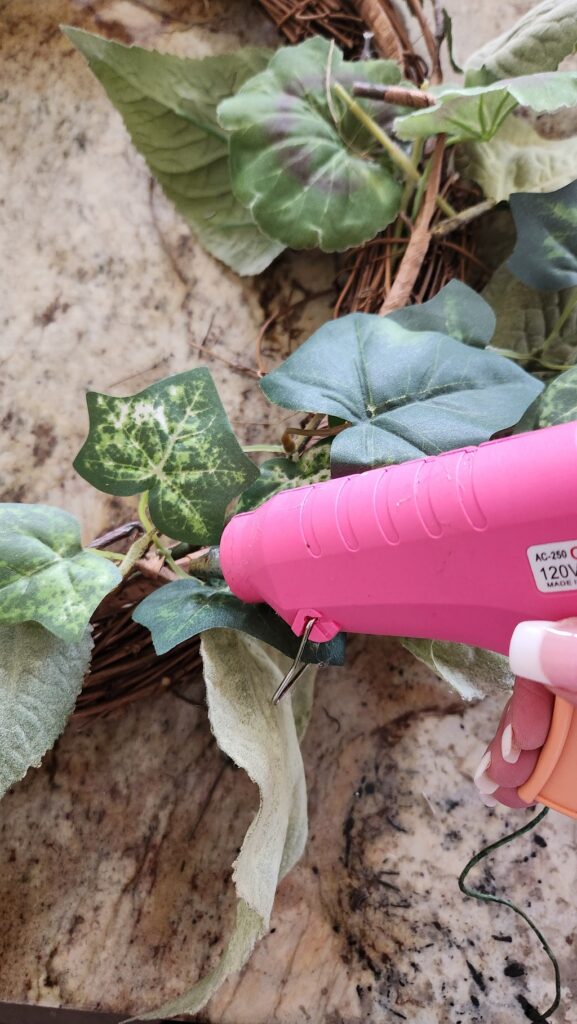 greenery being glued on wreath with glue gun