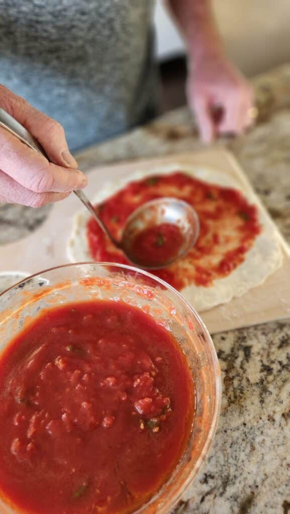pizza sauce being ladled onto pizza dough