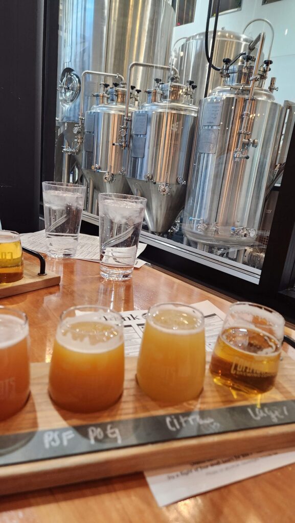 beer flight with brewery vats in background