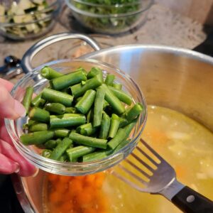 ladies hand putting in bowl of green beans into soup pot