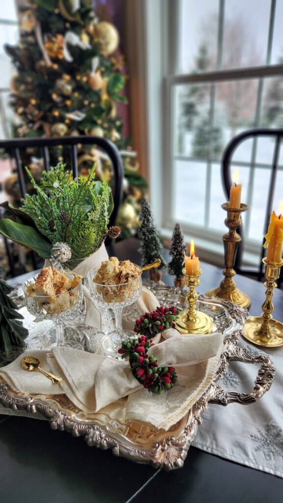 Silver tray with break pudding in goblets and brass candles holders with christmas tree in background