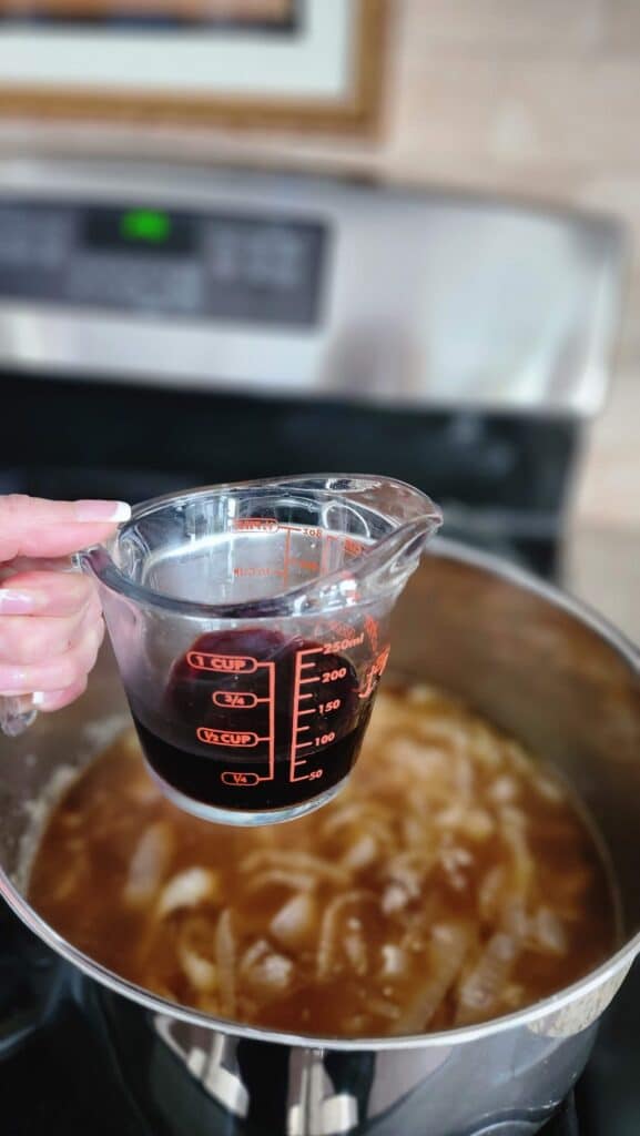 measure cup of red wine ready to add to a simmering pot of soup