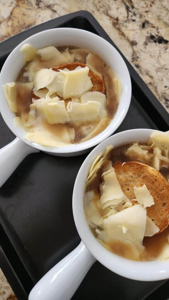 sliced cheese and bread added to small crock of soup ready to broil