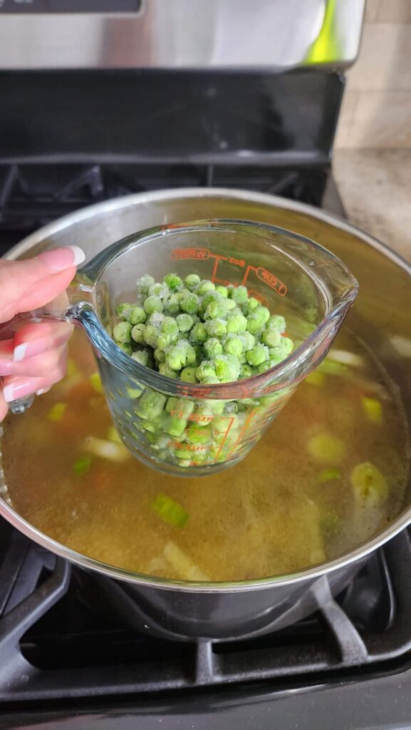 measuring cup with frozen peas over a stock pot