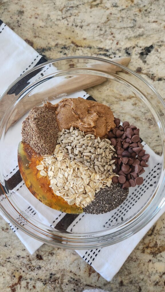 glass mixing bowl with oats, chocolate chips, honey and almond butter ingredients