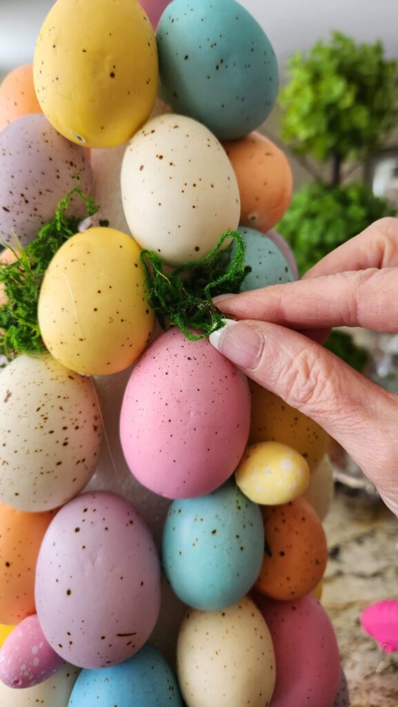 green moss being added between eggs on topiary tree