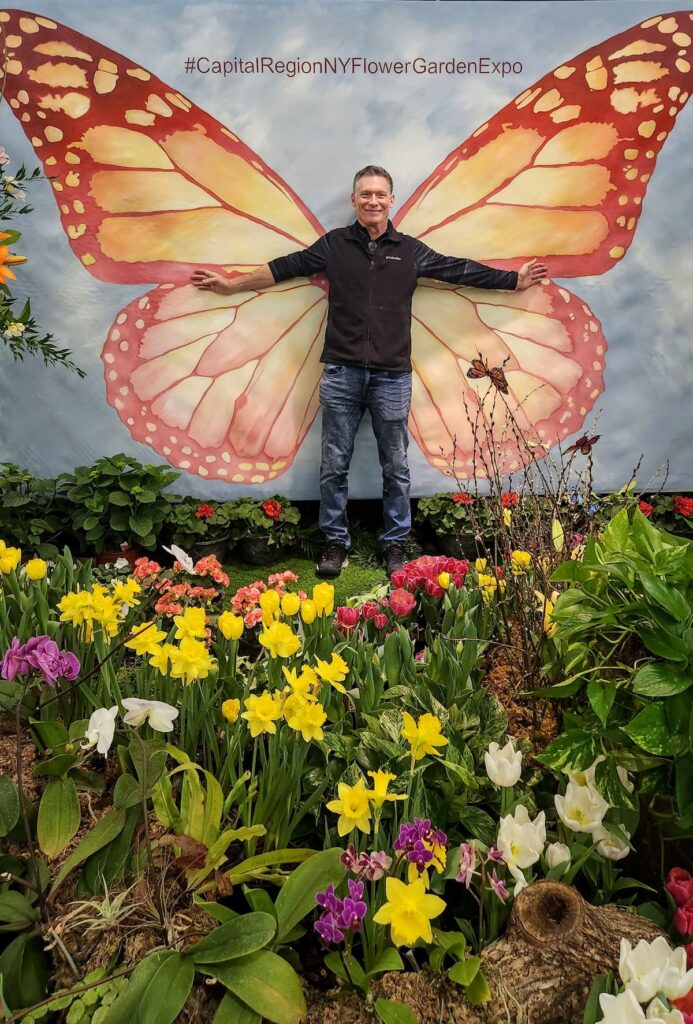 man in front of butterfly wall mural at garden show