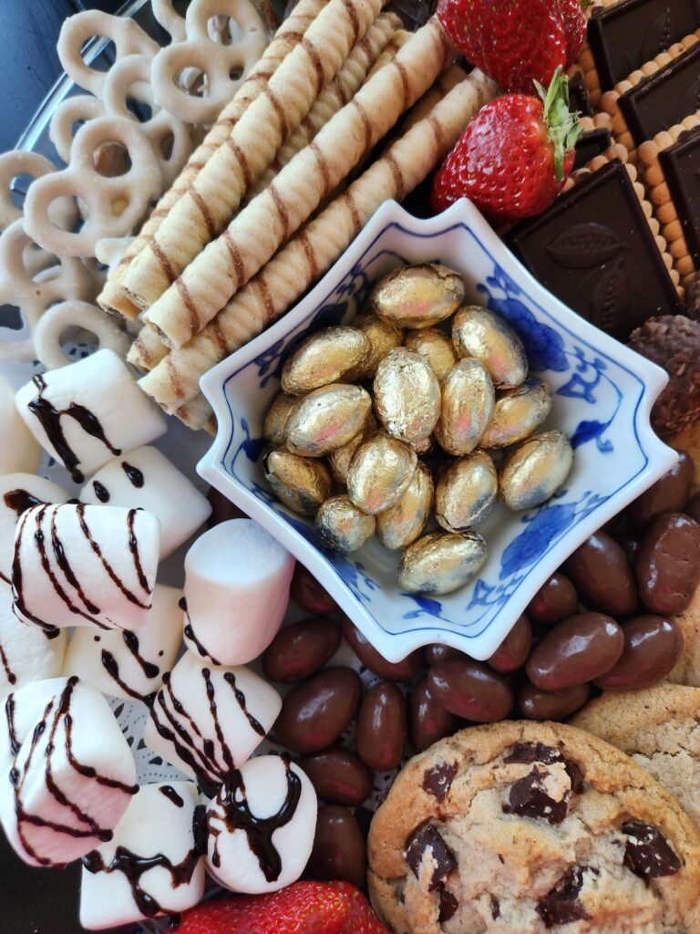 marshmellows drizzled with chocolate with bowl of gold foiled candy in bowl