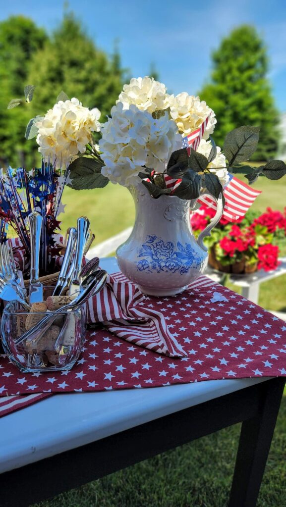 vintage blue and white pitcher on table with white hydrangea in it and amerian flags for memorial day