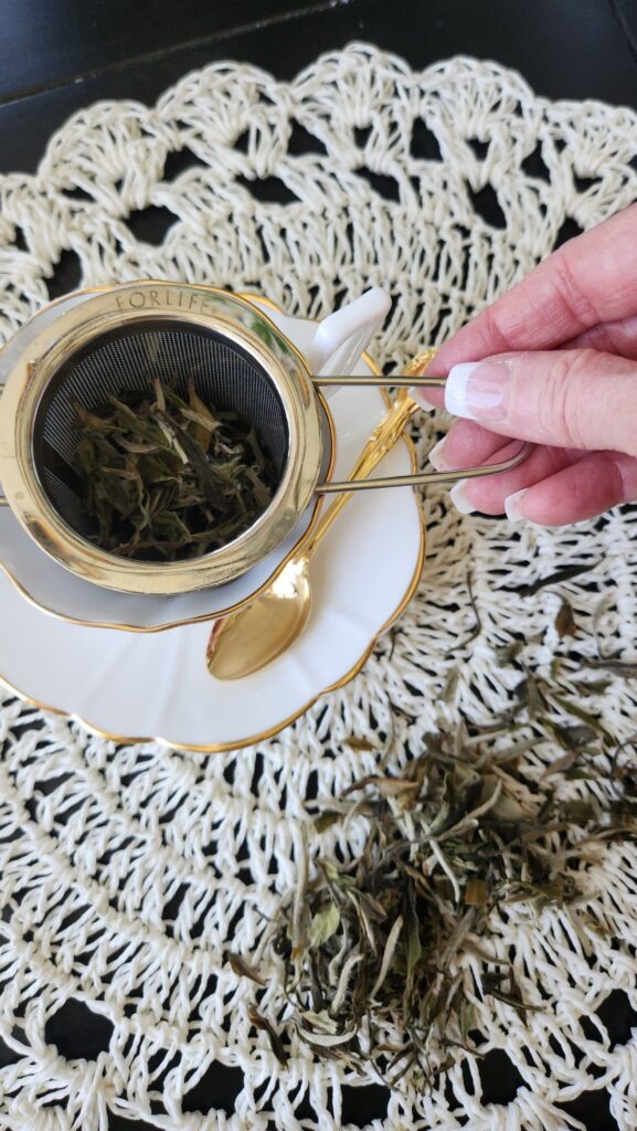 ladies hand holding tea strainer over white tea cup