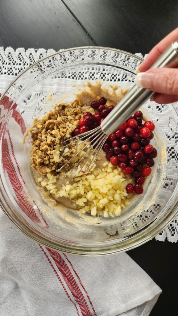 glass bowl with apples, walnuts and cranberries being mixed into batter