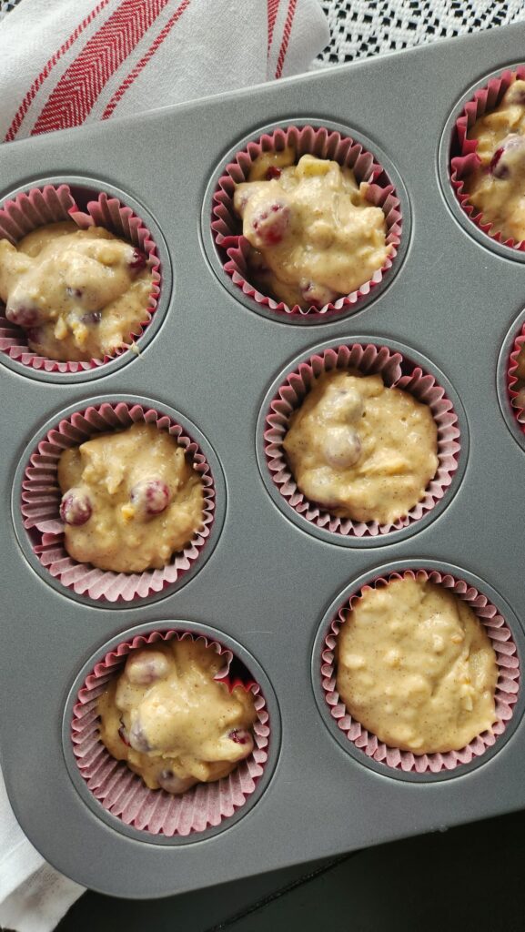 muffin tin with cranberry walnut muffin batter in it