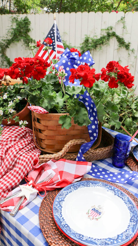 outdoor table with blue checked tablecloth and a wicker basket filled with red geraniums for memorial day