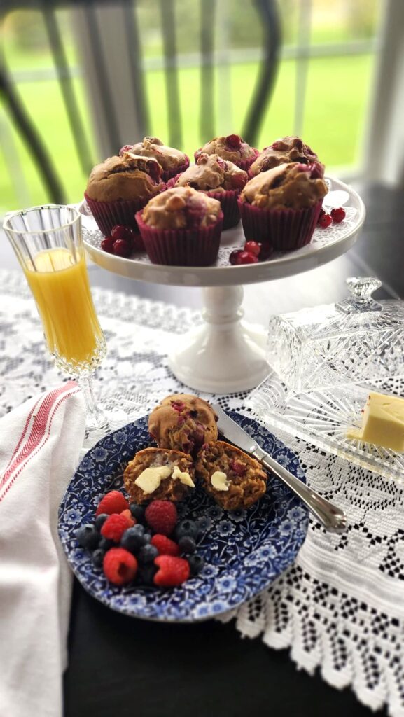 cranberry walnut muffins on a white pedestal dish with orange juice and butter dish on the side