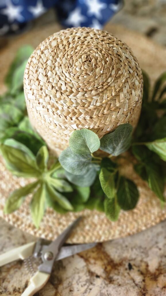 faux greenery attached around the straw hat 