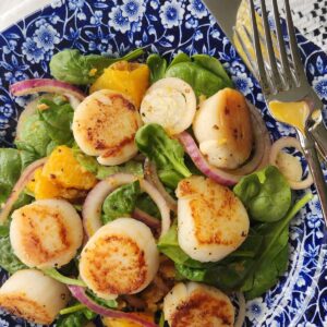 close up of orange scallop salad on blue and white dish