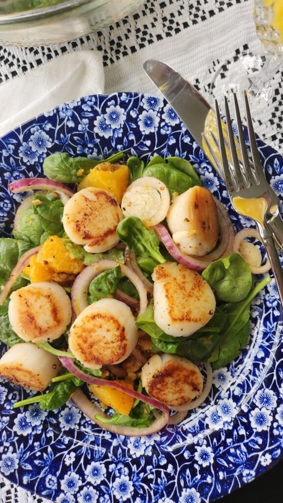 close up of orange scallop salad on blue and white dish