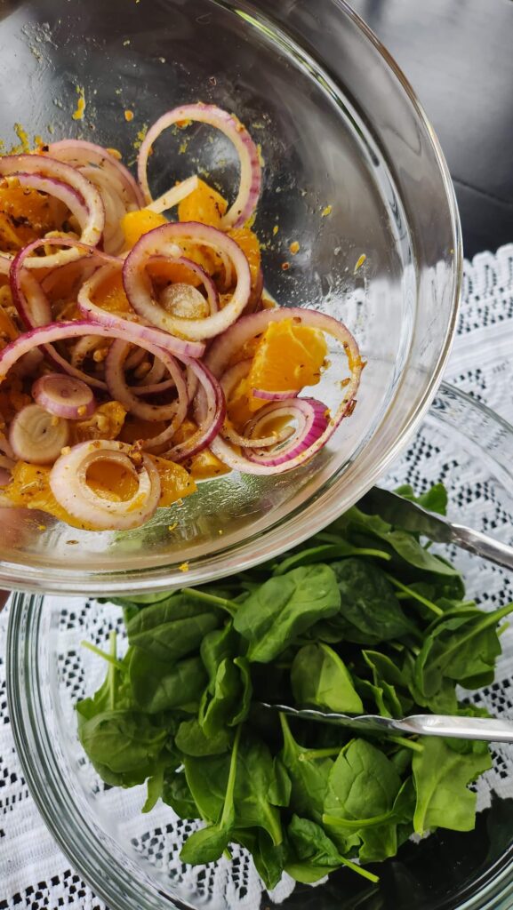 Glass bowl with spinach with another glass bowl on top with oranges, onions and dressing ready to be added