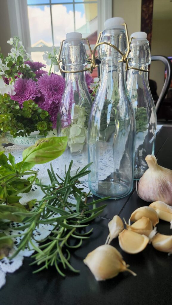 empty glass bottles on table with garlic and herbs ready to make insfused olive oil