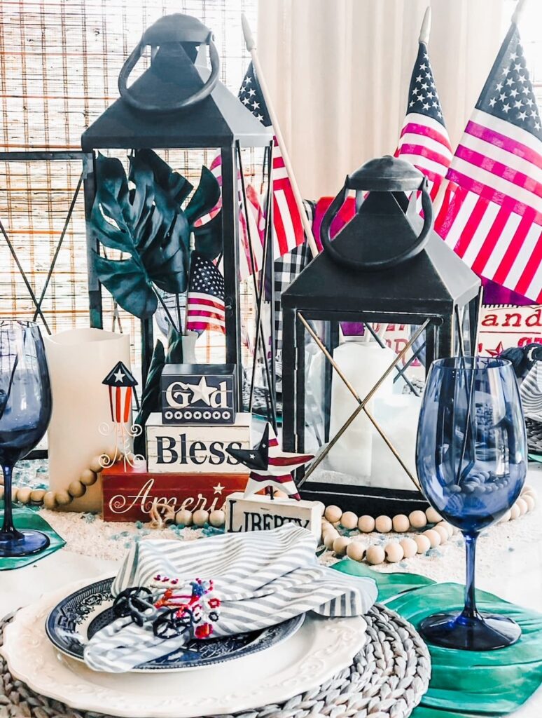 memorial day table set with a black lantern, blue and white dishes and god bless america stacked with wooden blocks