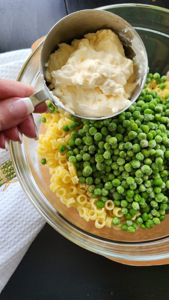 stainless measure cup with  mayonnaise over a bowl of pasta and peas