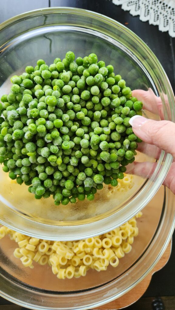 glass bowl of frozen peas over cooked pasta bowl