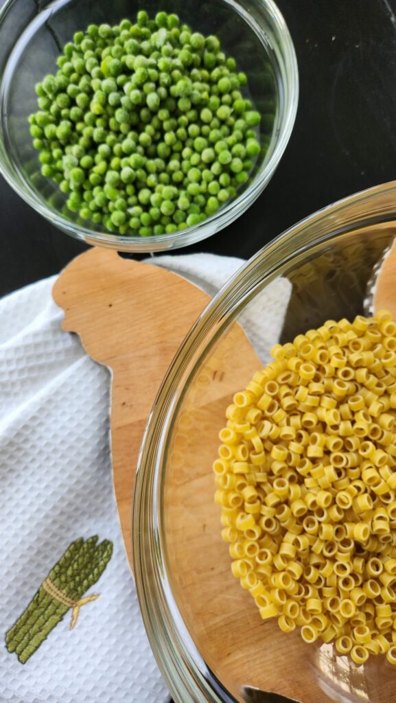 uncooked ring pasta in glass bowl with green peas in bowl next to it