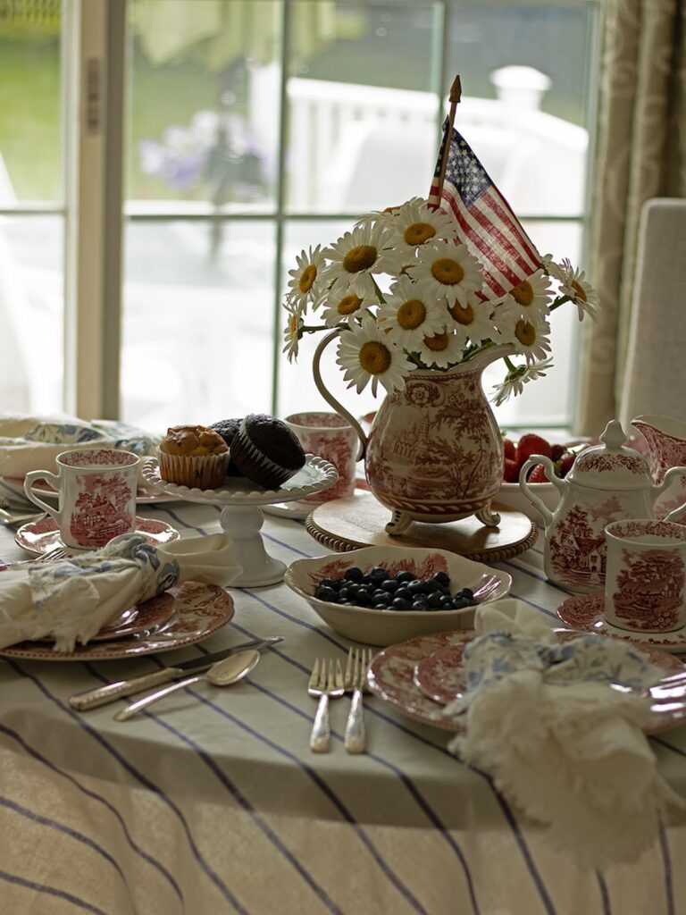 brunch table set with vintage dishes and pitcher with white daisies and american flag