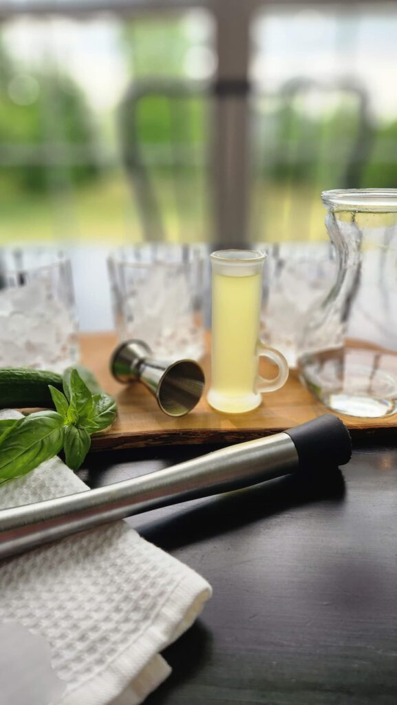 three glasses with ice, muddler, basil and cucumber on table ready to make a vodka smash cocktail