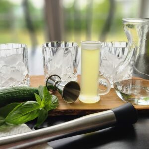 muddler with three glasses, basil and shot glass of limoncello to make a cocktail on a table