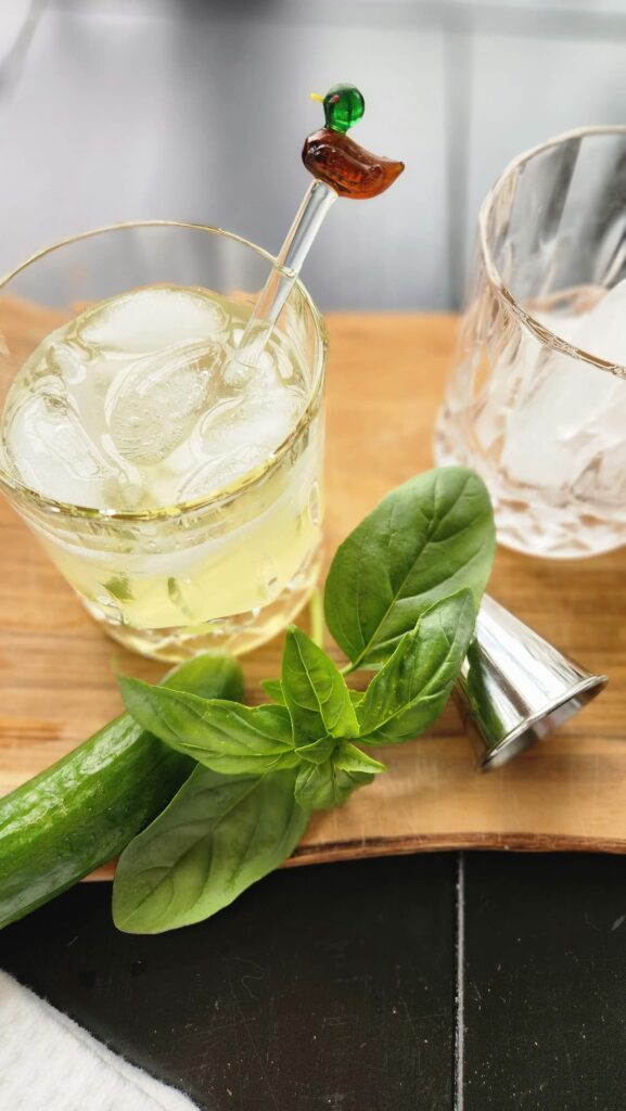 clear rock glass with ice and cucumber basil smash cocktail in it