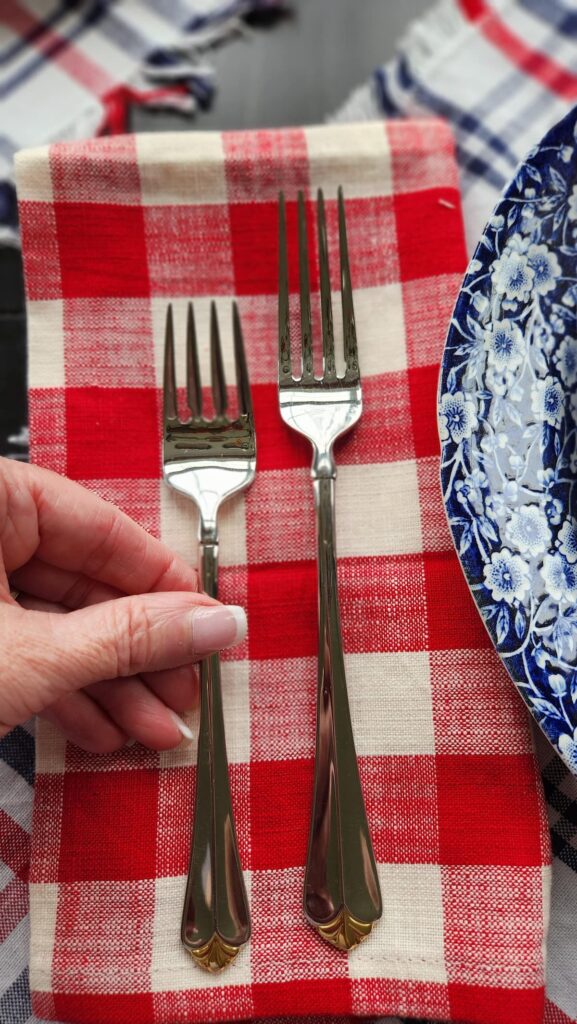 red and white checked cloth napkin with ladies hand placing a fork on it