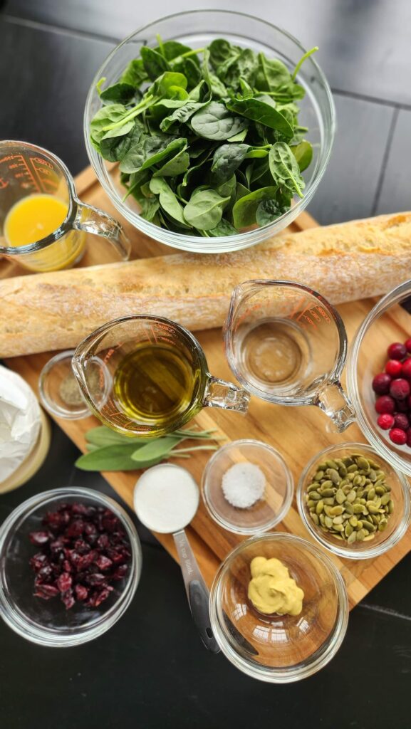 ingredients to make spinach cranberry salad on table with baguette bread