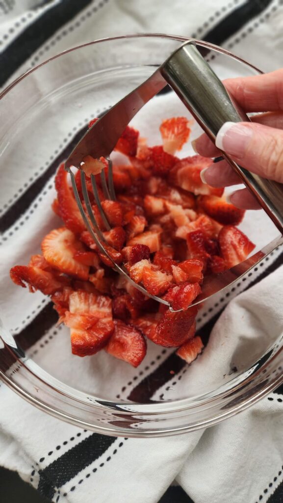 bowl of cut up strawberries with hand masher going to be used to mash berries