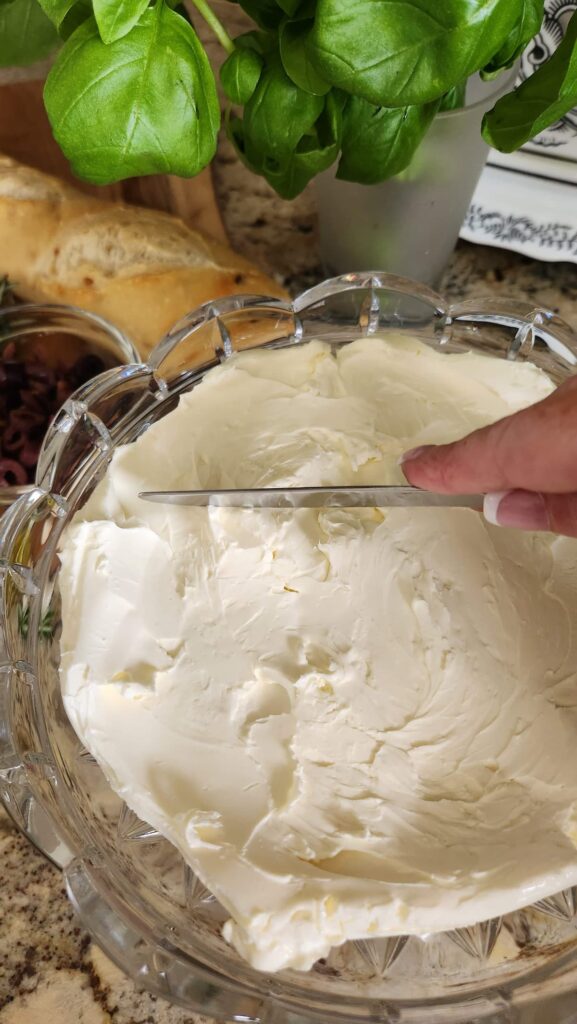 hand spreading the goat cheese on a glass serving dish