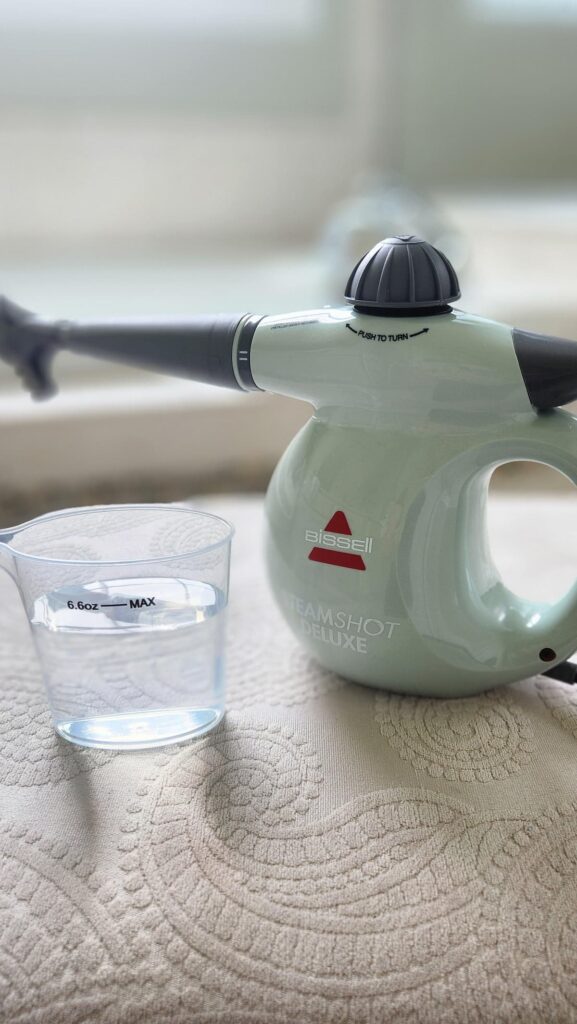 steam cleaner on upholstered stool with water cup next to it