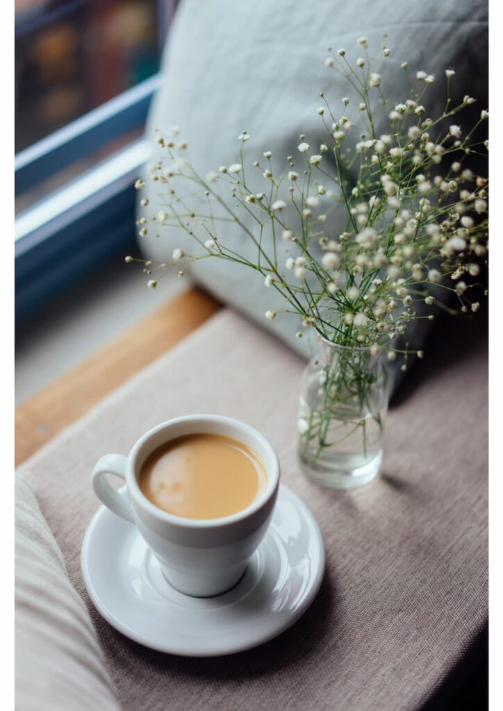 cup of coffee on table with vase of babies breath