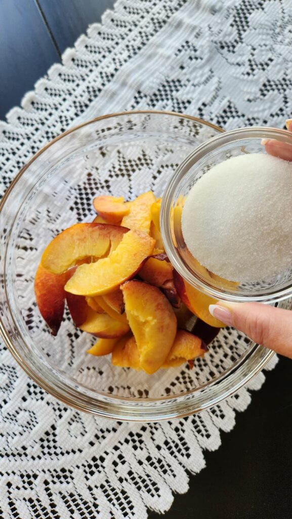 glass bowl of sliced nectarines with sugar being added