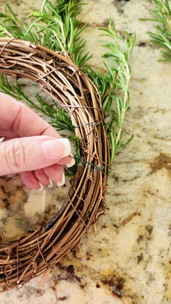 wrapping wire around the back of the grapevine wreath attaching the rosemary sprigs