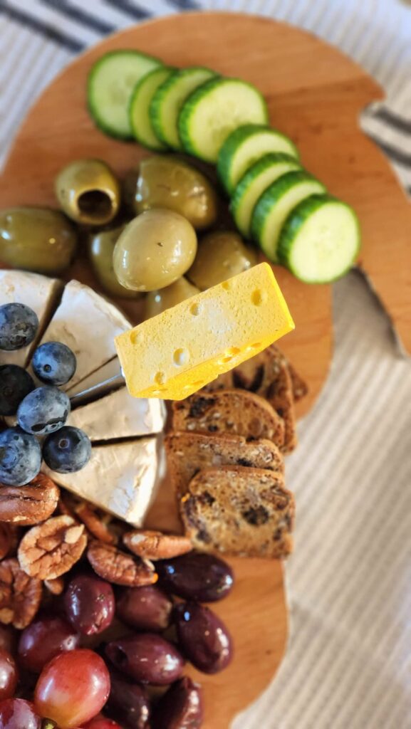 overhead of charcuterie board with brie cheese in triangles topped with blueberries, olives and sliced cucumbers