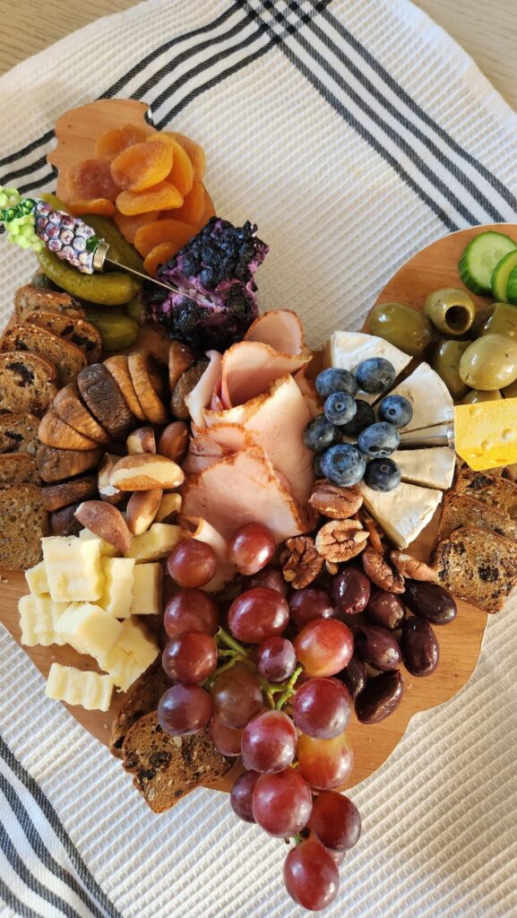 small charcuterie board with grapes, ham, blueberries, pickles, brie cheese, goat cheese and dried figs and more
