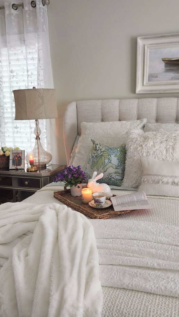 white bedding on bed with wicker tray, candle and flowers on tray