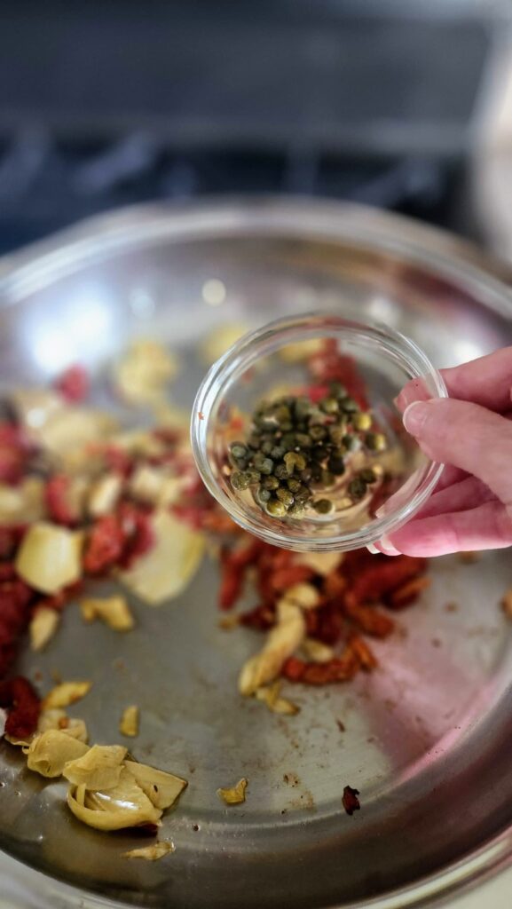 small glass bowl with capers ready to go into frying pan